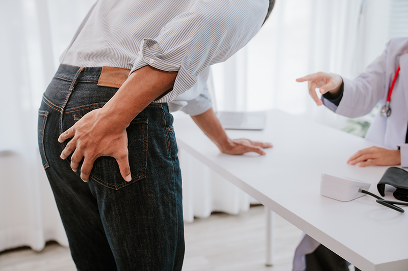 A person holding their lower back in discomfort, representing anal fistula pain